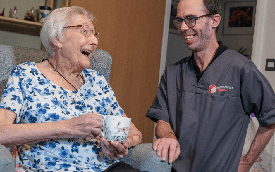 Image of a service user and a Care Assistant, smiling and laughing whilst holding a cup of tea.