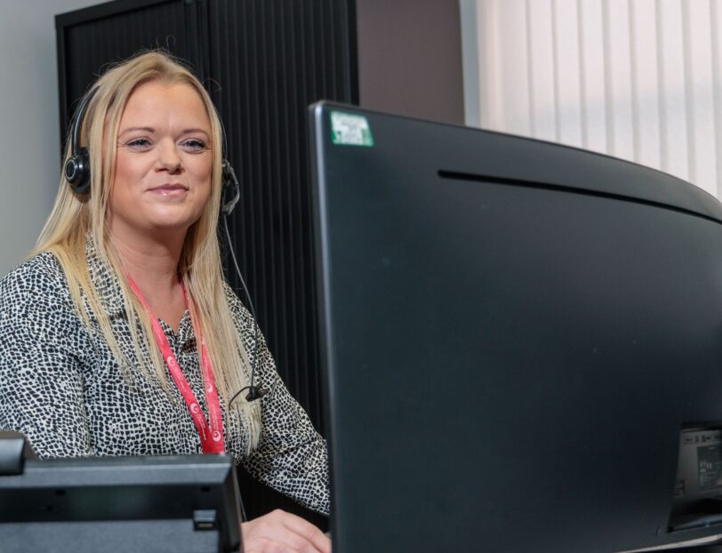 An image of a woman sat at a desk with a headset on.