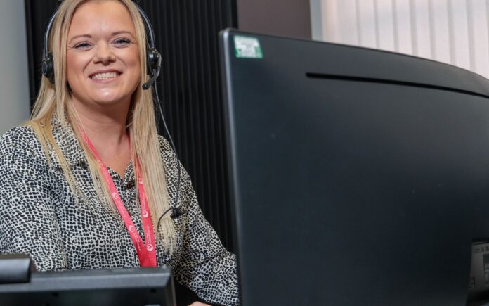 An image of a woman sat at a desk with a headset on.
