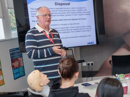Group of people in a classroom, with a trainer at the head of the table, leading a powerpoint.