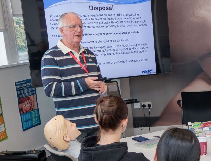 Group of people in a classroom, with a trainer at the head of the table, leading a powerpoint.