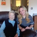 An image of one service user and a Care Assistant on a couch, smiling and laughing with each other.