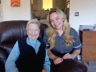 An image of one service user and a Care Assistant on a couch, smiling and laughing with each other.