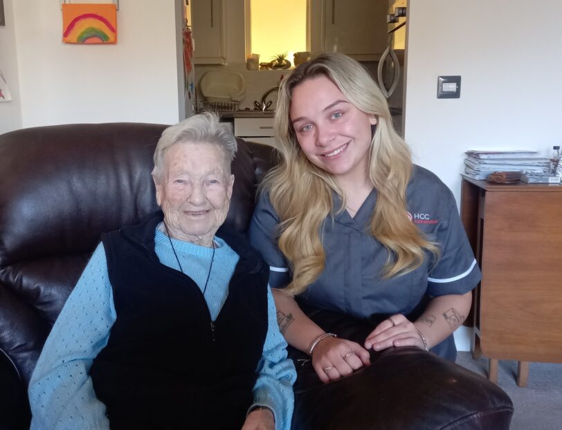 An image of one service user and a Care Assistant on a couch, smiling and laughing with each other.