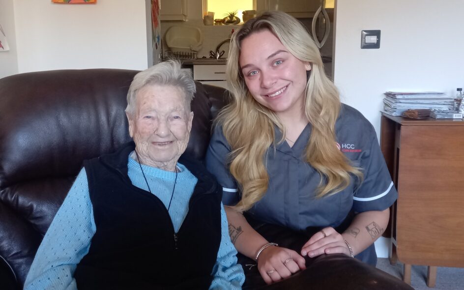 An image of one service user and a Care Assistant on a couch, smiling and laughing with each other.