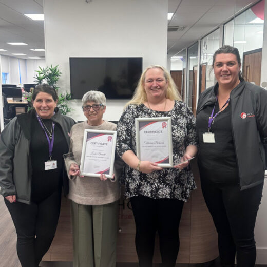 Image of 4 individuals in an office setting, carrying certificates.