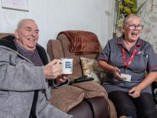 Image of a service user and a Care Assistant, smiling and laughing whilst holding a cup of tea.