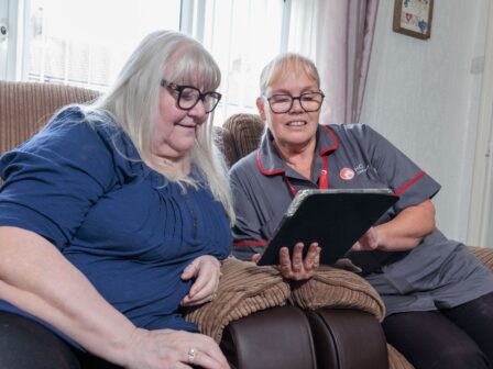 An image of one service user and a Care Assistant on a couch, smiling and laughing with each other.