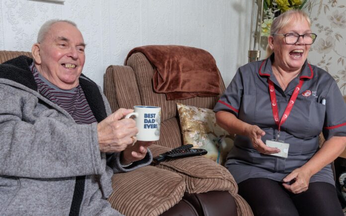 Image of a service user and a Care Assistant, smiling and laughing whilst holding a cup of tea.