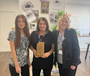3 people in an office setting, holding up a bronze award.