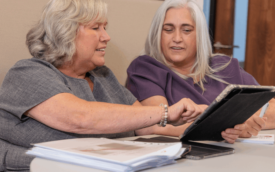 A man and a woman in an office setting taking part in a meeting, smiling whilst looking at a tablet. Understanding Care leading with care