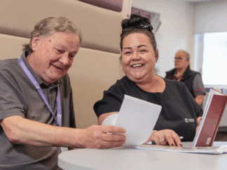 A man and a woman in an office setting taking part in a meeting, laughing and smiling at each other whilst looking at a piece of paper.