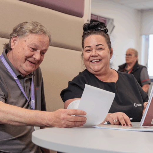 A man and a woman in an office setting taking part in a meeting, laughing and smiling at each other whilst looking at a piece of paper.
